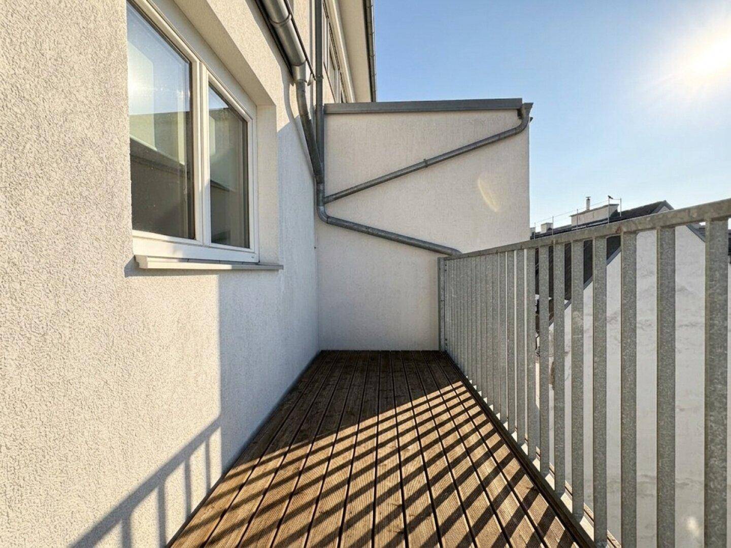 Schmaler Balkon mit Holzboden und weißer Fassade, bietet einen privaten Außenbereich.