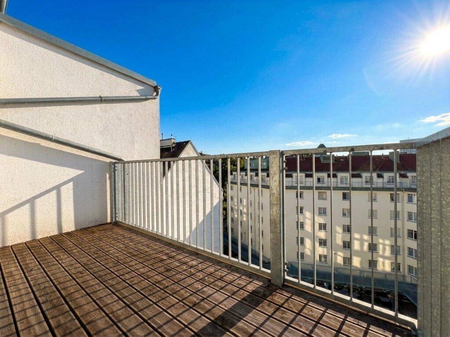 Sonniger Balkon mit Holzboden und Blick auf die umliegenden Gebäude, ideal zum Entspannen im Freien.