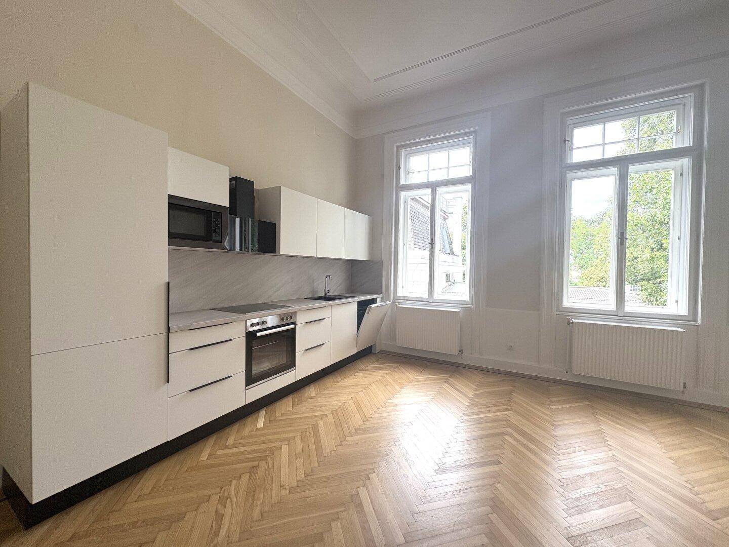 Helle Einbauküche mit weißen Schränken, modernen Geräten und Blick aus großen Fenstern.