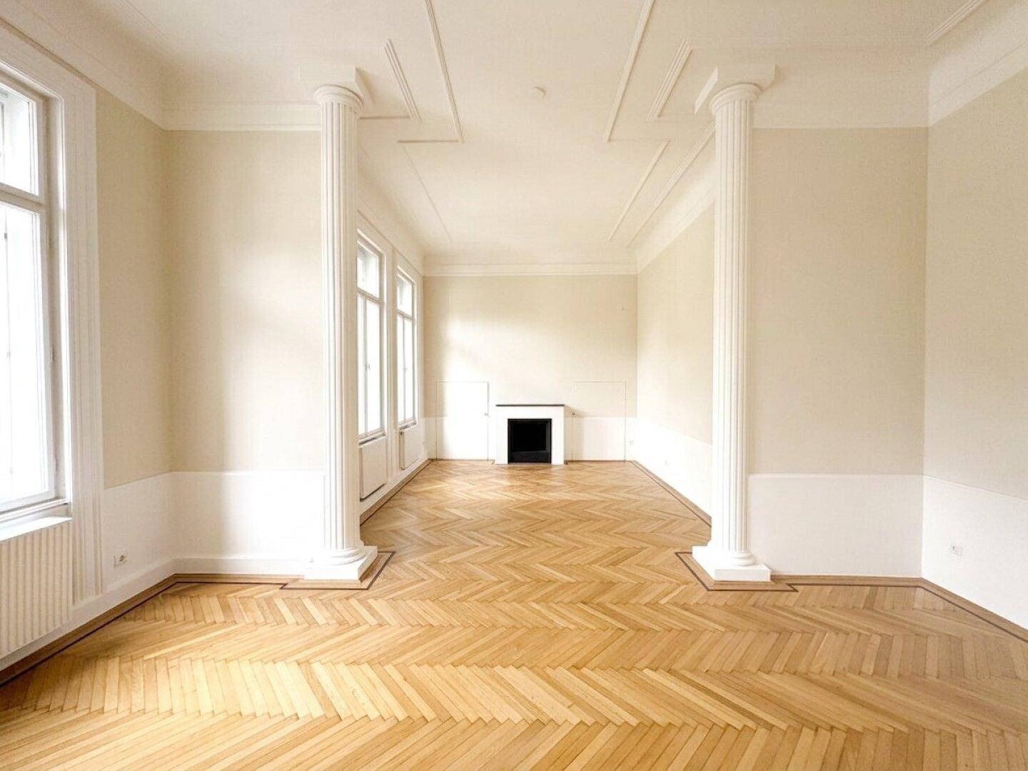 Elegantes Wohnzimmer mit Fischgrätparkett, hohen Decken, dekorativen Säulen und einem Zierkamin.