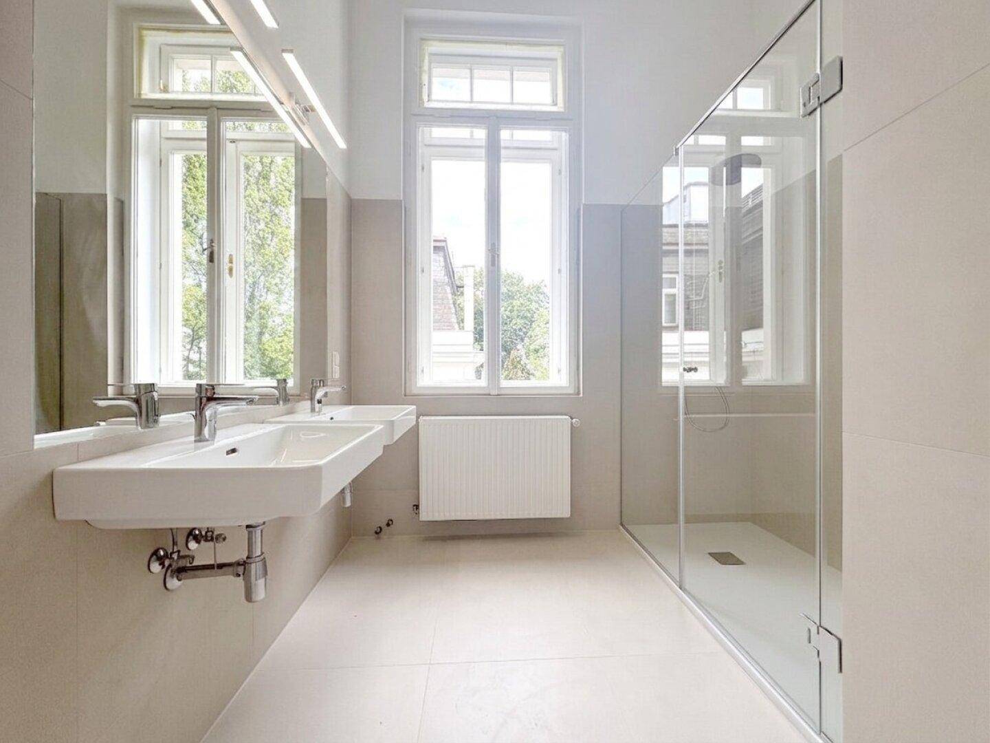 Modernes Badezimmer mit Doppelwaschbecken, großer begehbarer Dusche und Fenster für Tageslicht.