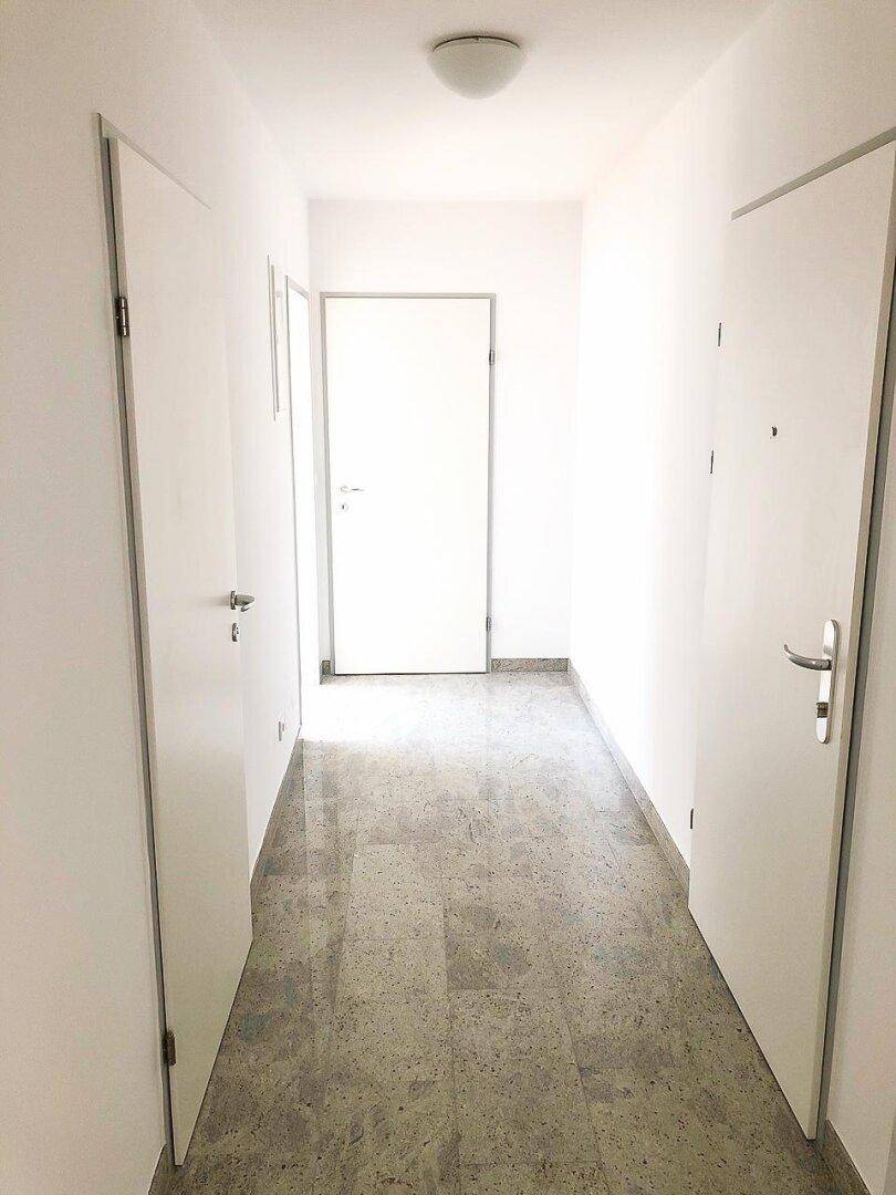 Heller Flur mit hellgrauem Fliesenboden und weißen Türen, der zu weiteren Räumen führt.