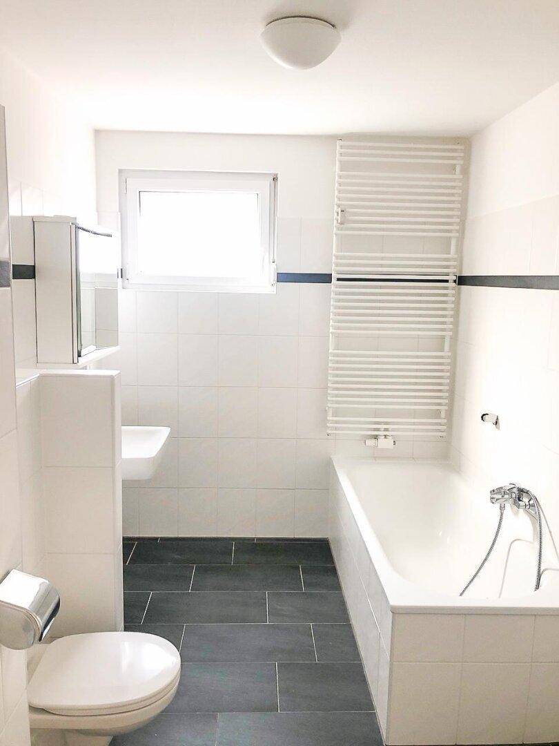 Modernes Badezimmer mit Badewanne, WC, Waschbecken, Fenster und beheiztem Handtuchhalter.