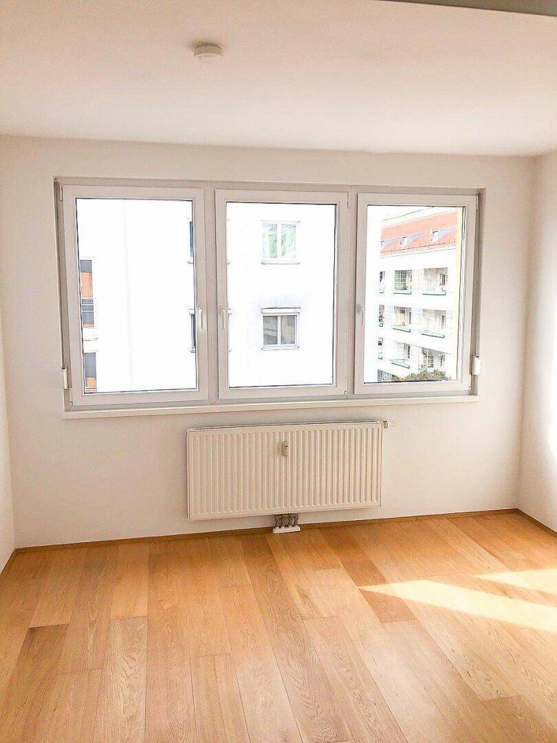 Geräumiges Zimmer mit hellem Holzparkettboden und großen Fenstern, die einen Blick auf die Stadt bieten.