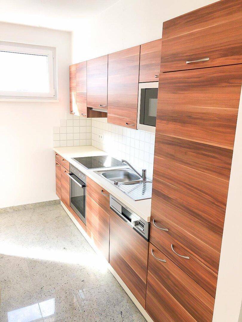 Funktionale Küche mit Holzschränken, integrierten Geräten und einem Fenster für natürliches Licht.