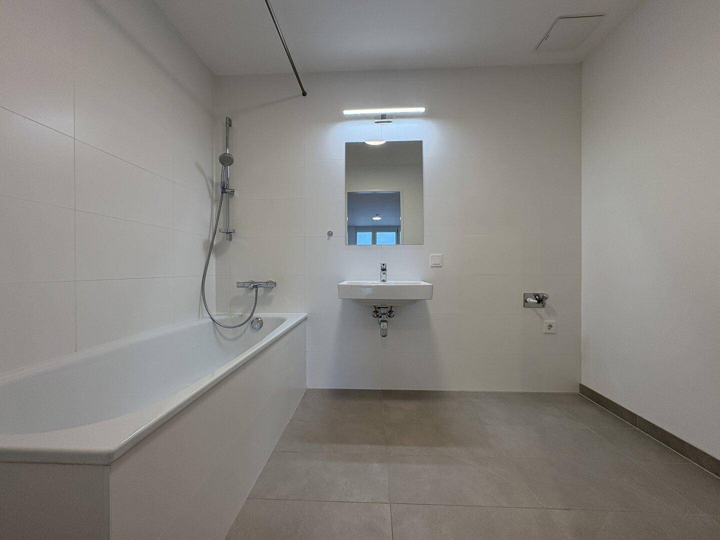 Modernes Badezimmer mit Badewanne, Waschbecken und großformatigen Fliesen.