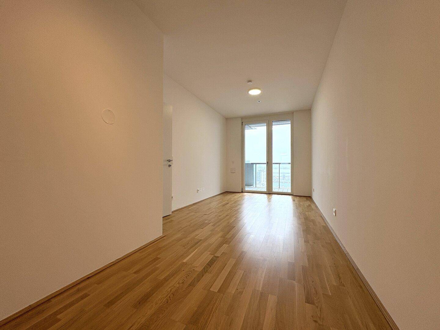 Langer, heller Wohnraum mit Parkettboden und großen Fenstern zum Balkon.