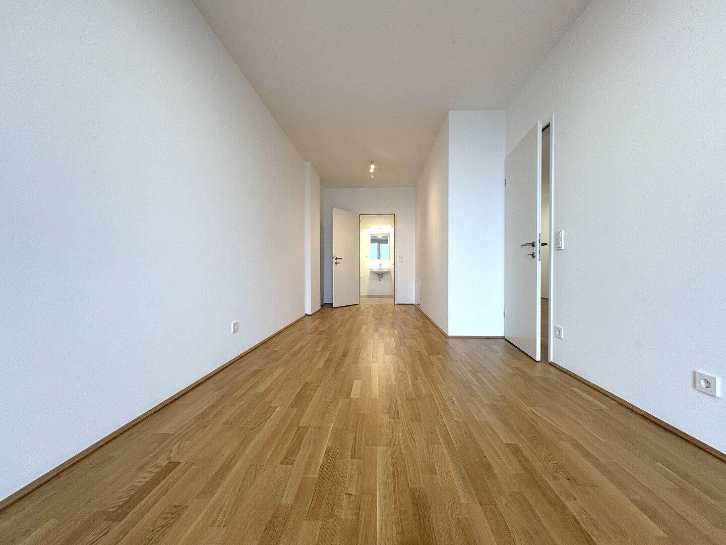 Heller Flur mit Parkettboden, der zu einem modernen Badezimmer führt.