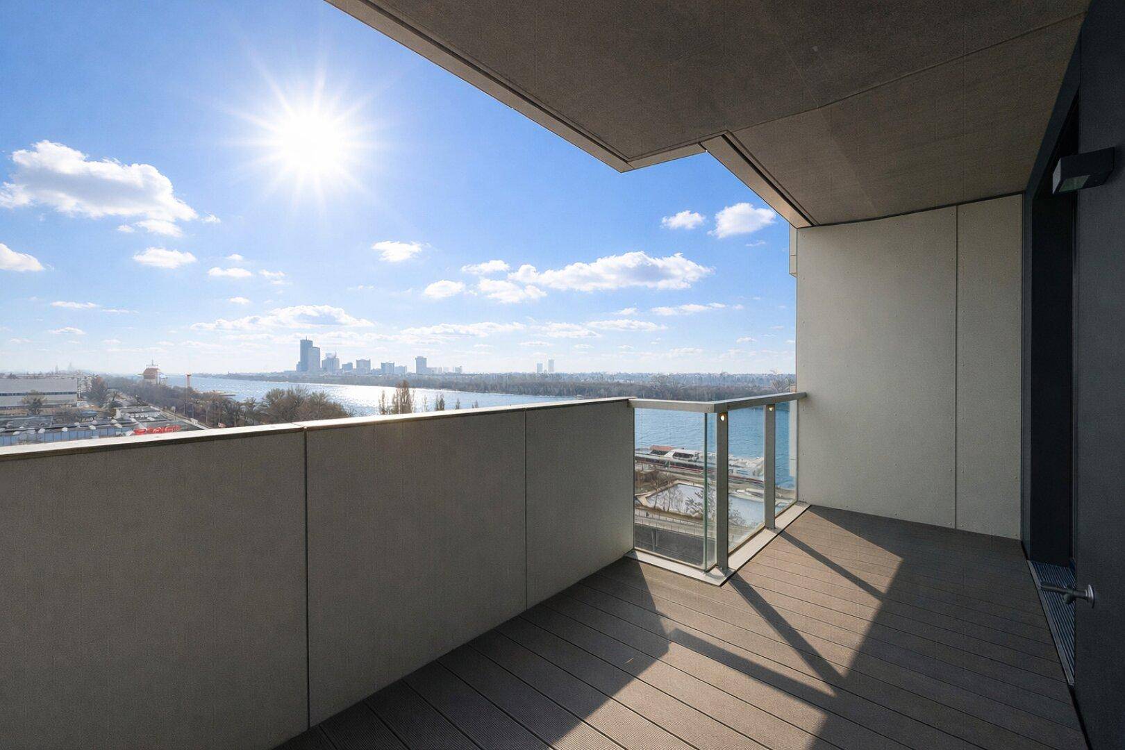 Sonniger Balkon mit Holzboden und weitem Blick über den Fluss und die Stadt.