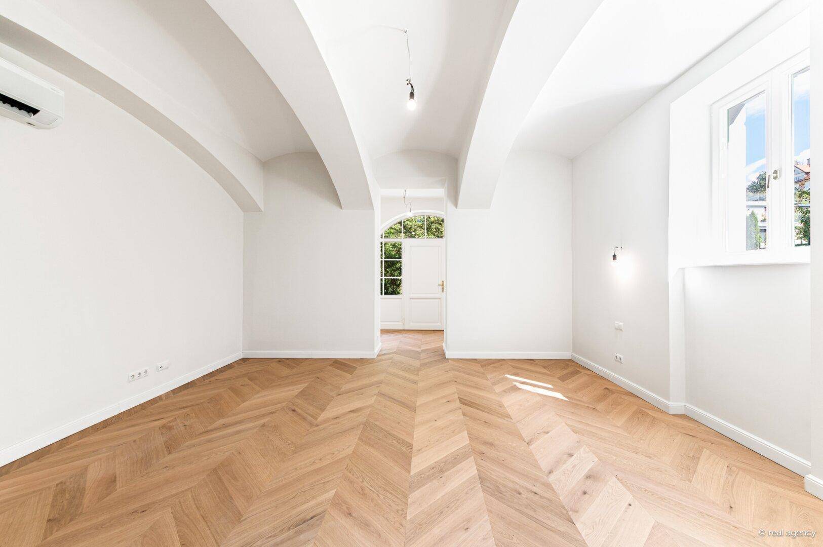 Heller Raum mit Fischgrätparkett, hohen Decken und Klimaanlage, ideal als Wohn- oder Schlafzimmer.