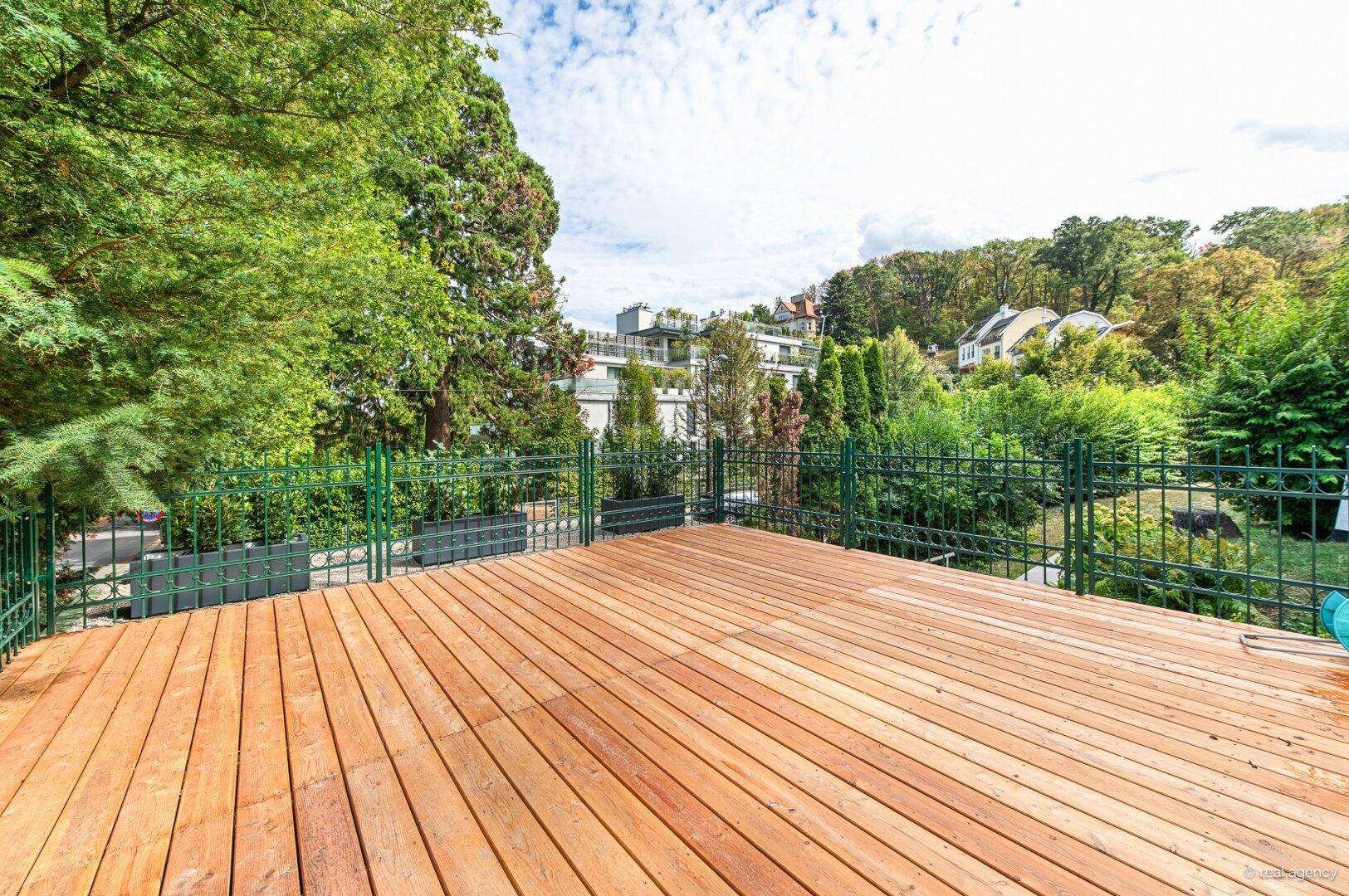 Geräumige Holzterrasse mit weitem Blick auf die grüne Umgebung und umliegende Häuser.
