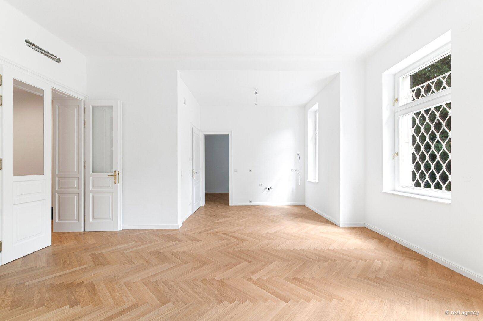Geräumiges Zimmer mit Fischgrätparkett, hohen Decken und doppelten Flügeltüren.