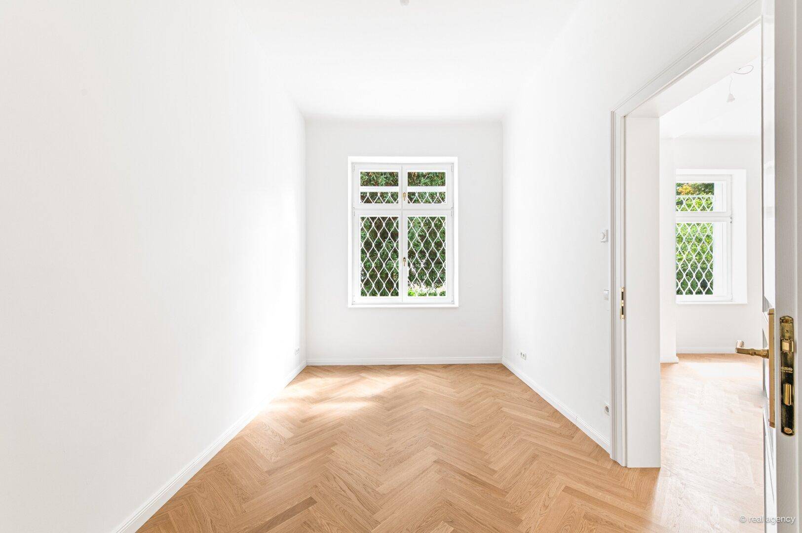 Kleineres Zimmer mit Fischgrätparkett und Fenster mit Blick ins Grüne.