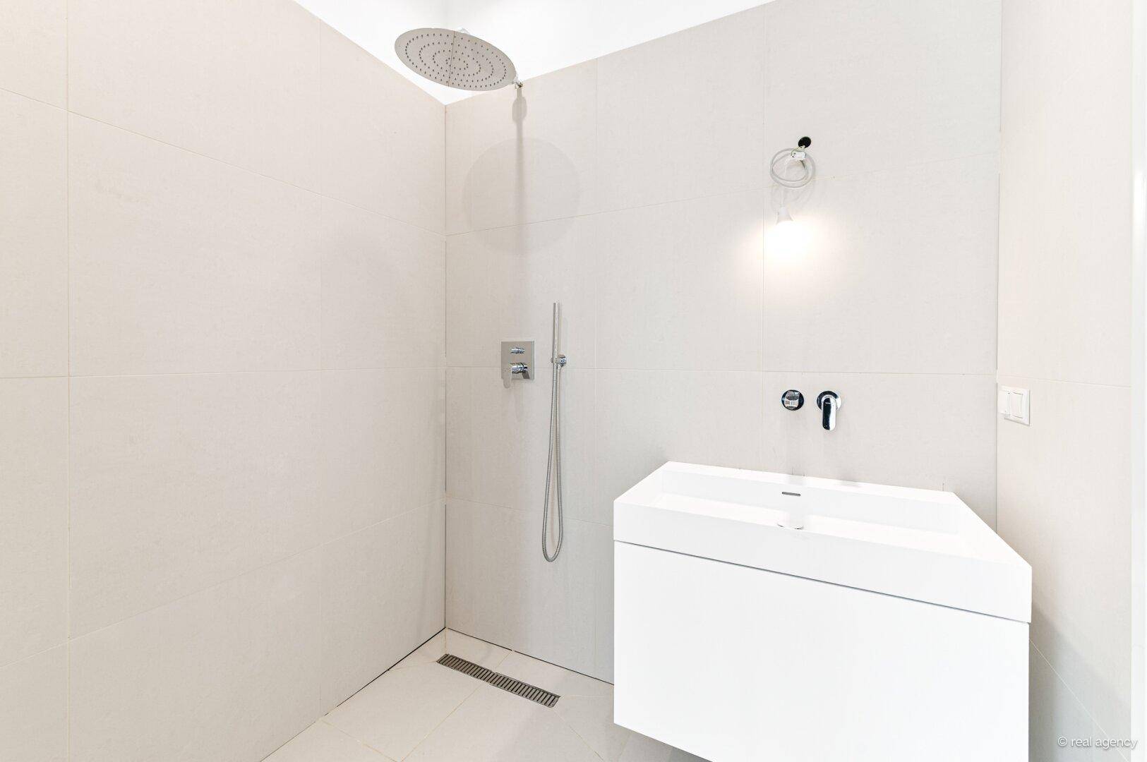 Modernes Badezimmer mit großer begehbarer Dusche und minimalistischem Waschbecken.