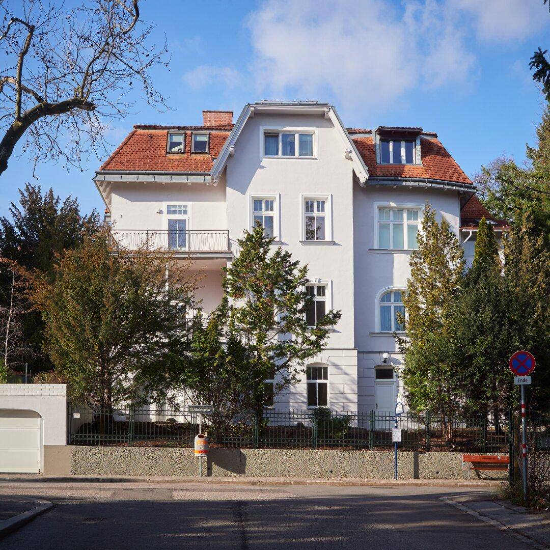 Elegantes klassisches Gebäude mit weißer Fassade und rotem Ziegeldach, umgeben von Bäumen.