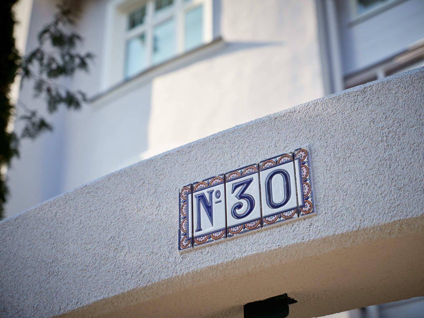 Nahaufnahme der dekorativen Hausnummer "N° 30" an der Fassade des Gebäudes.