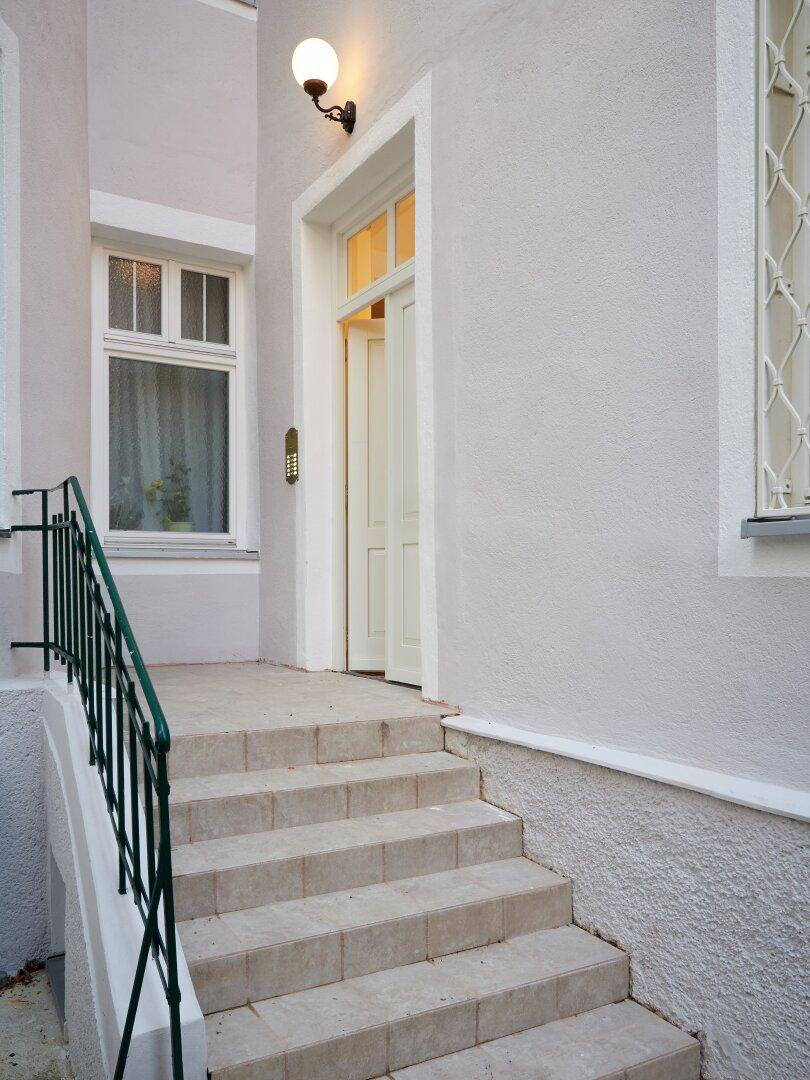 Eingangsbereich mit Steintreppe und grünem Geländer, führt zur Haustür.