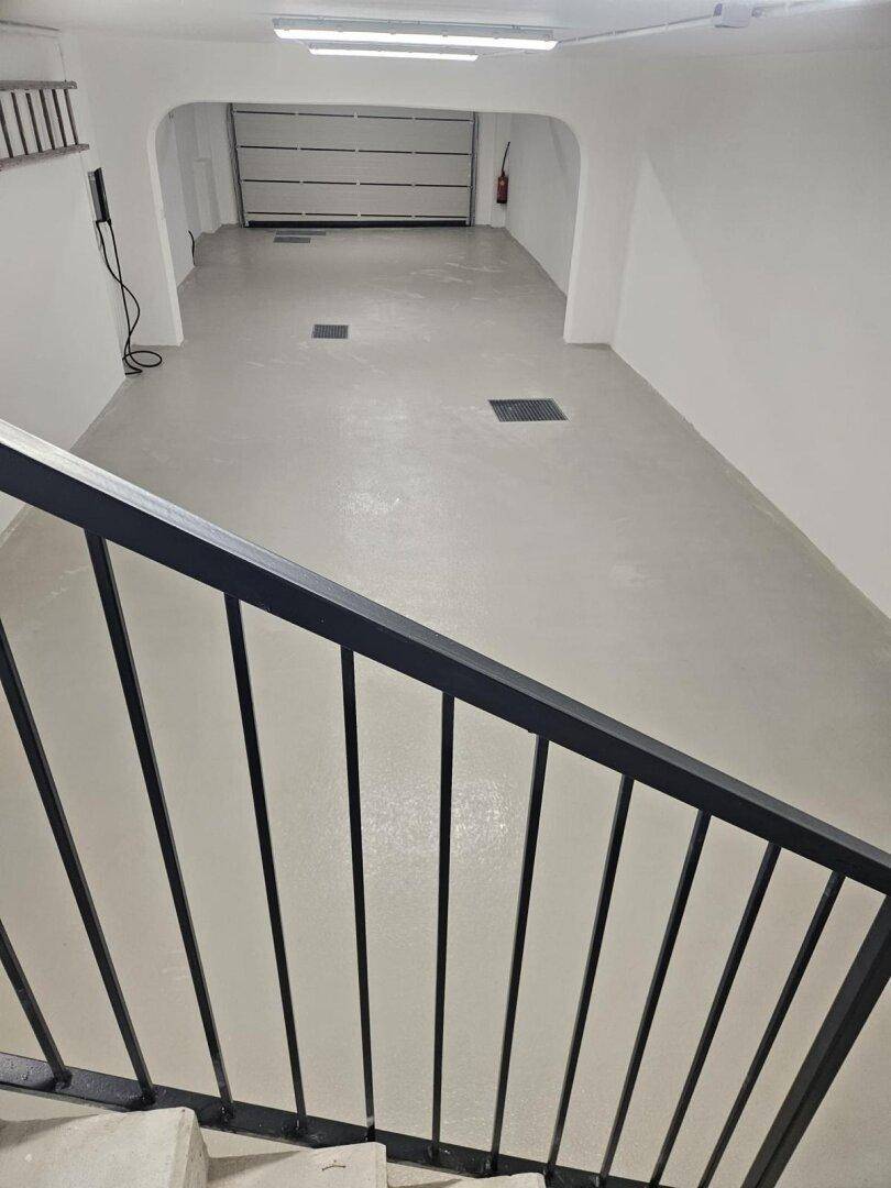 Geräumige Tiefgarage mit hellem Boden und Rolltor, von einer Treppe aus gesehen.