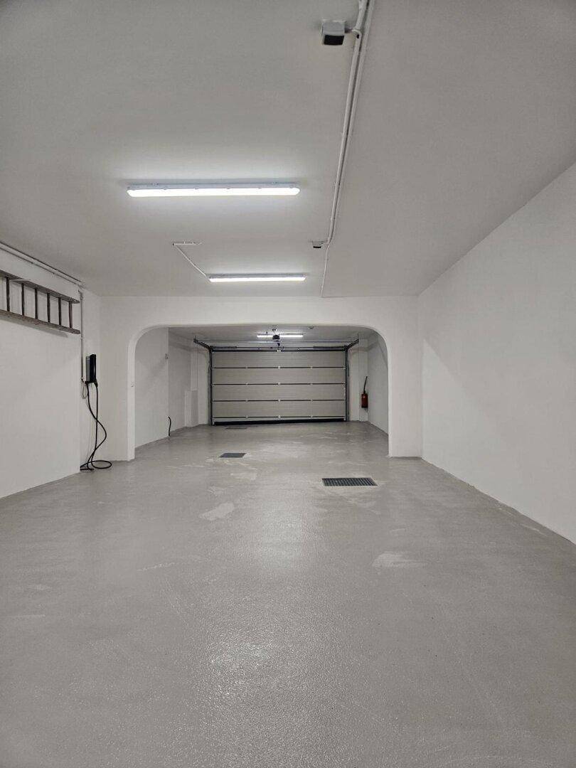 Weitläufige und helle Garage mit Rolltor und moderner Beleuchtung, inklusive Ladestation.