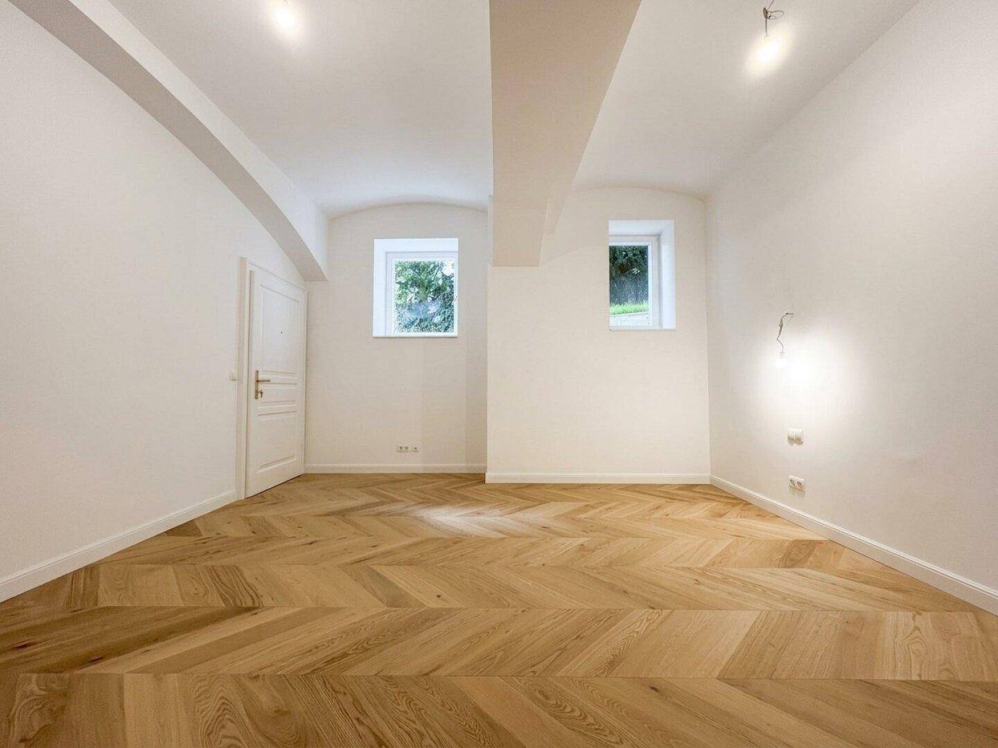 Heller Raum mit Fischgrätparkettboden und weißen Wänden, bereit zur individuellen Gestaltung.
