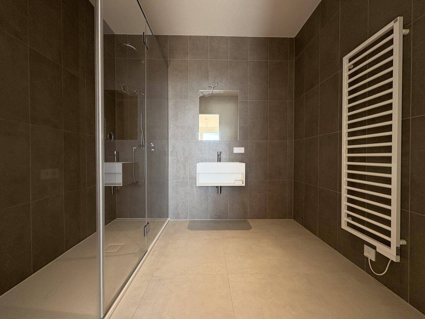 Modernes Badezimmer mit großen Fliesen, ebenerdiger Dusche und beheiztem Handtuchhalter.