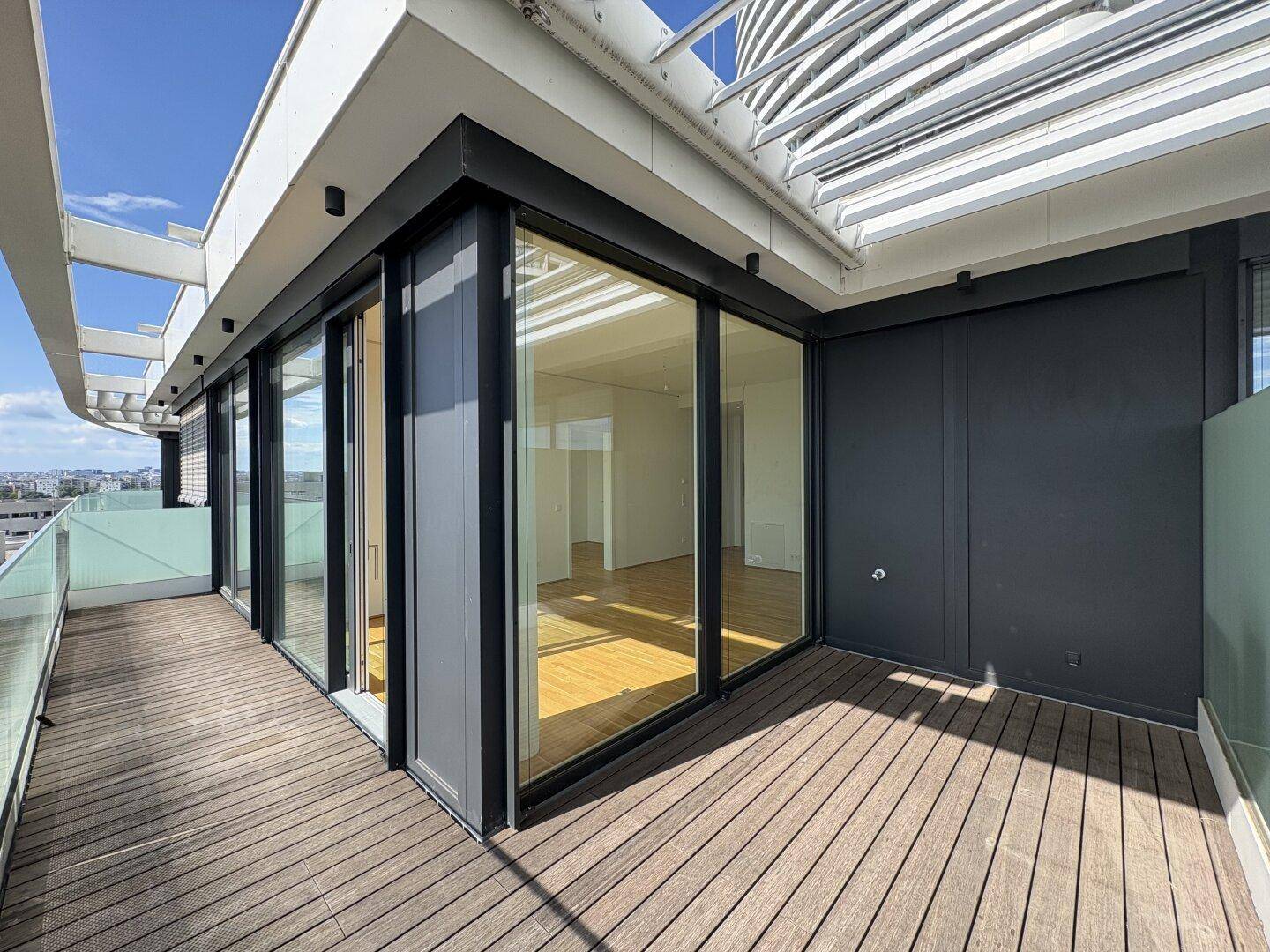 Großzügige Terrasse mit Holzdeck, Glasgeländer und weitem Blick über die Stadt und das Wasser.
