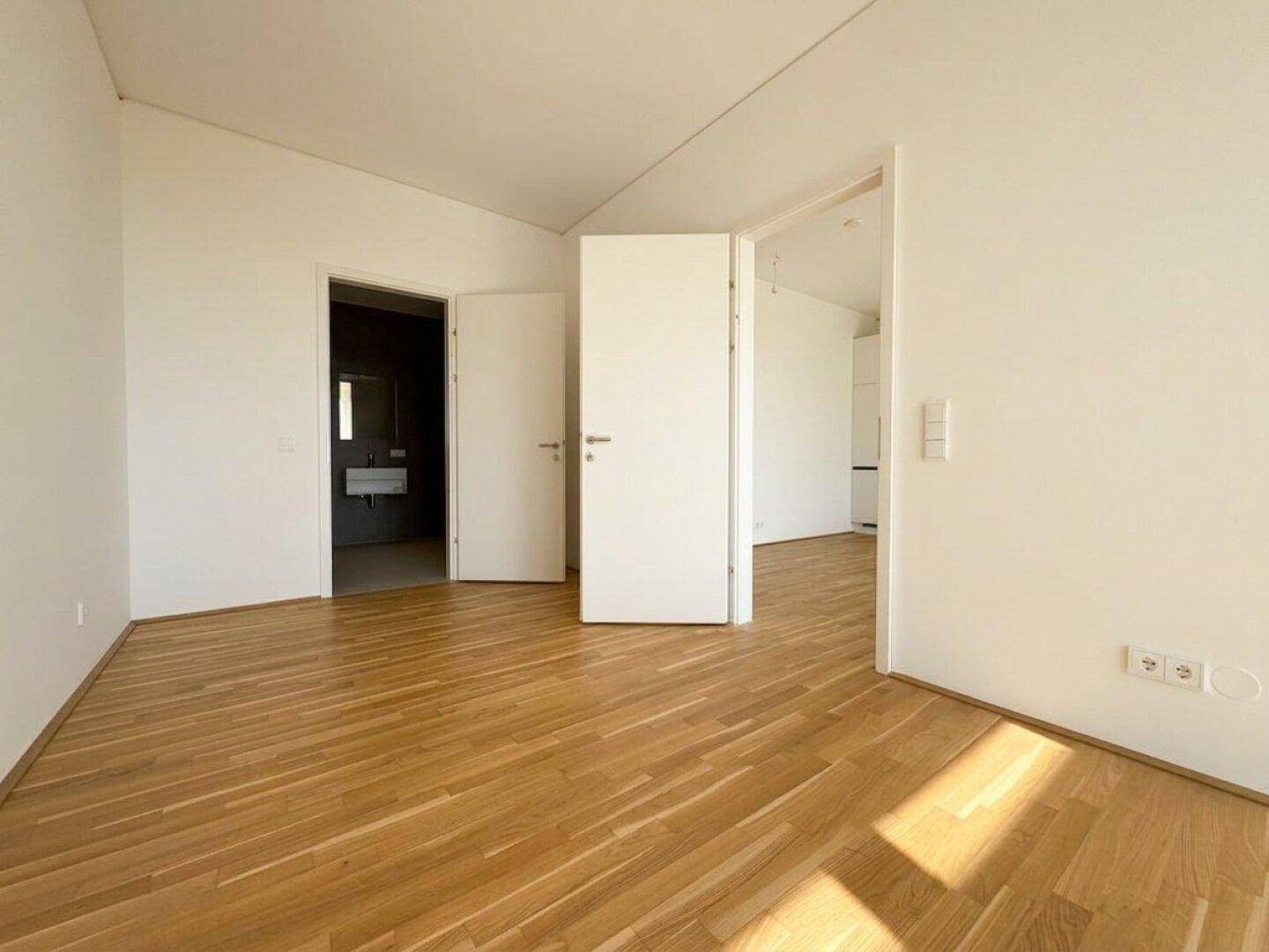Geräumiger, heller Raum mit Holzboden und Zugang zu einem modernen Badezimmer.