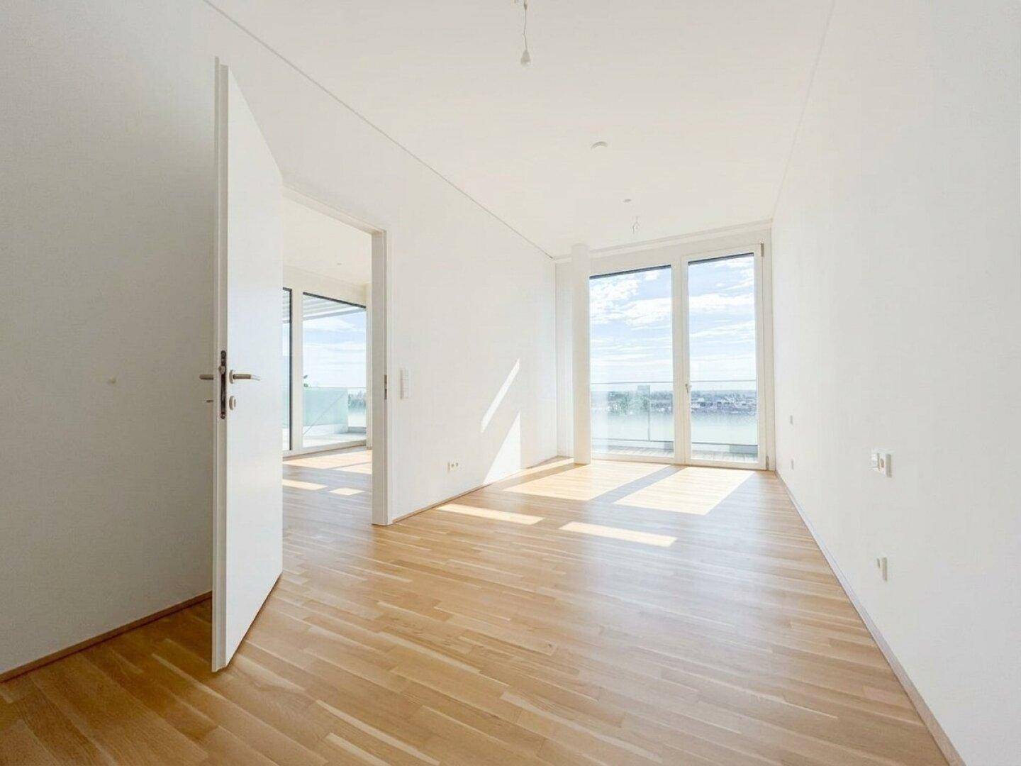Heller Wohnraum mit Holzboden und raumhohen Fenstern, die viel Tageslicht hereinlassen.
