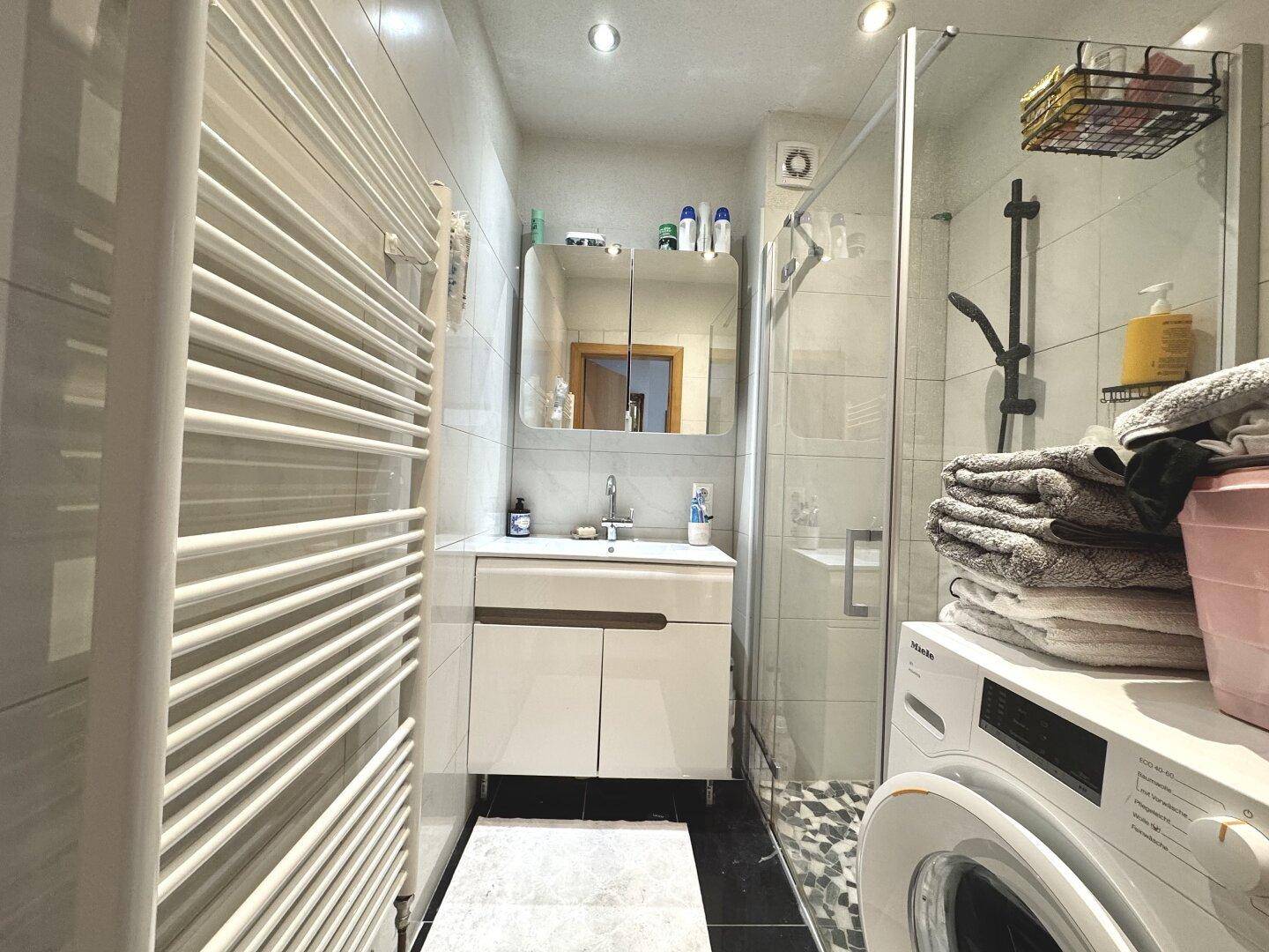 Modernes Badezimmer mit Duschkabine, Waschbecken und integrierter Waschmaschine.