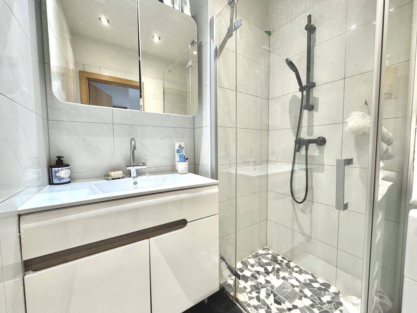 Helles Badezimmer mit moderner Duschkabine, Waschbecken und Spiegelschrank.