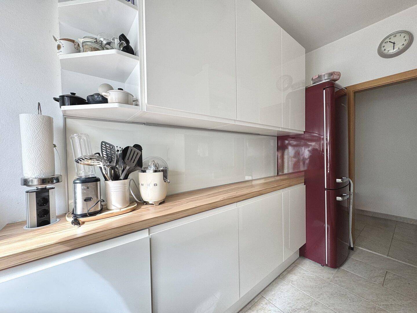Moderne Küche mit weißen Schränken, Holzarbeitsplatte und einem roten Retro-Kühlschrank.