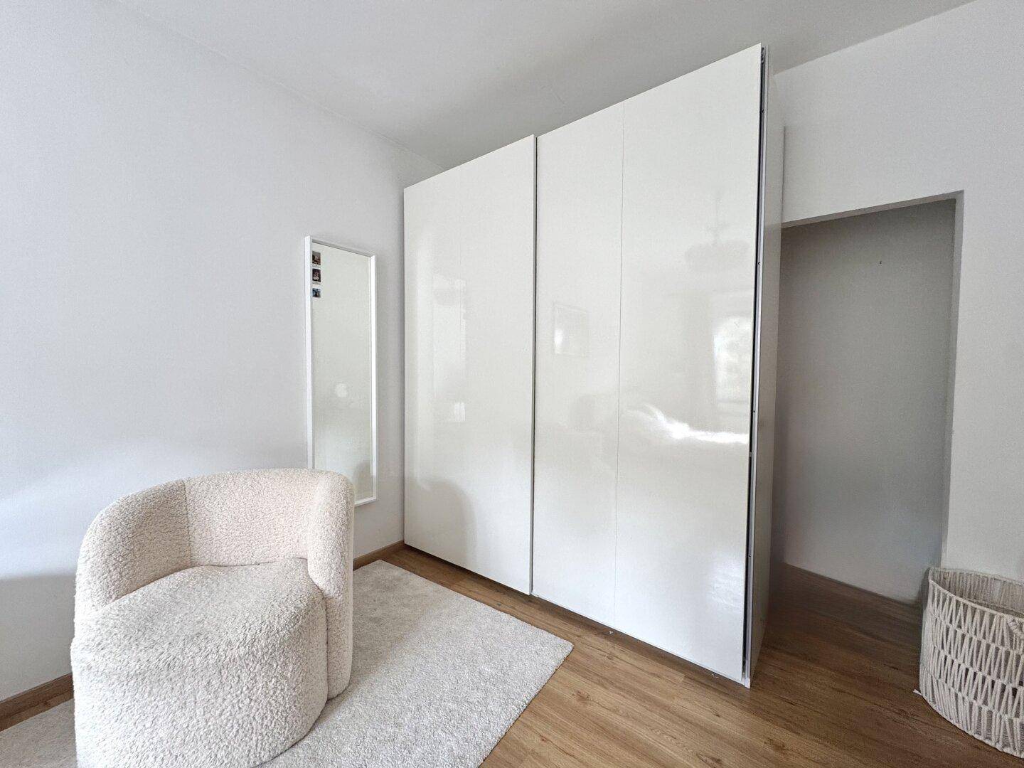 Schlafzimmerbereich mit großem weißen Kleiderschrank und einem gemütlichen Sessel.