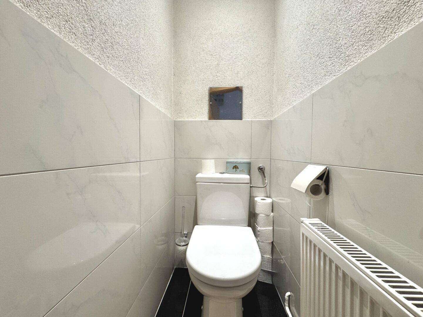 Separates WC mit Wandfliesen, Toilette und Heizkörper.