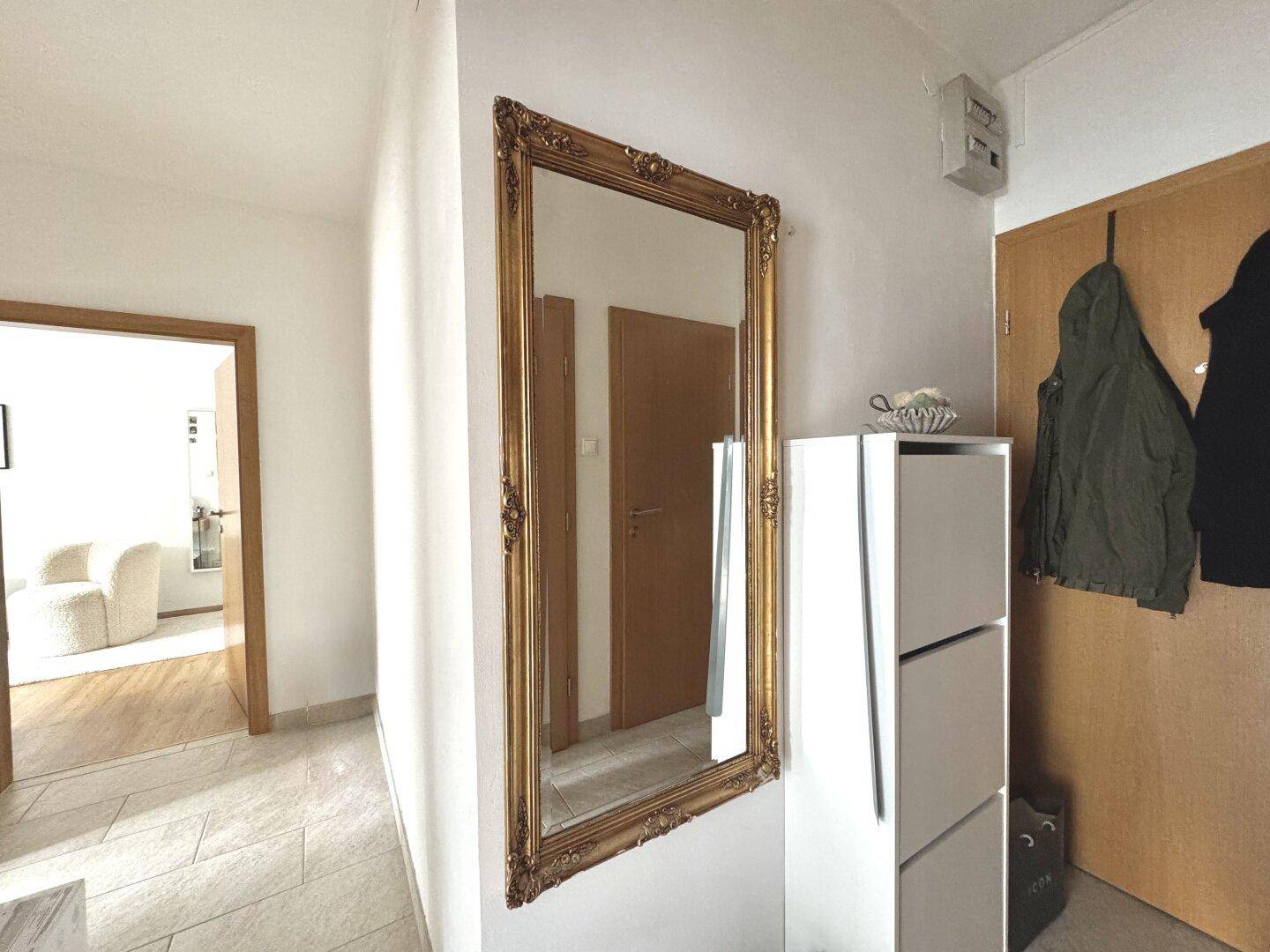 Eingangsbereich mit einem großen, verzierten Spiegel und Schuhschrank.