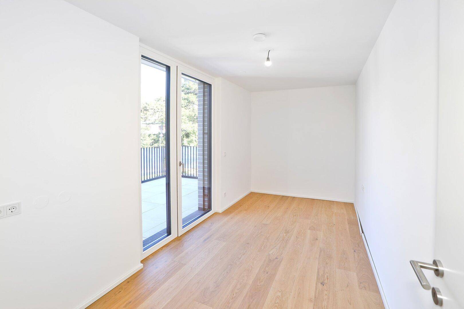 Leeres Zimmer mit Holzboden und Zugang zu einem Außenbereich, ideal als Schlaf- oder Arbeitszimmer.