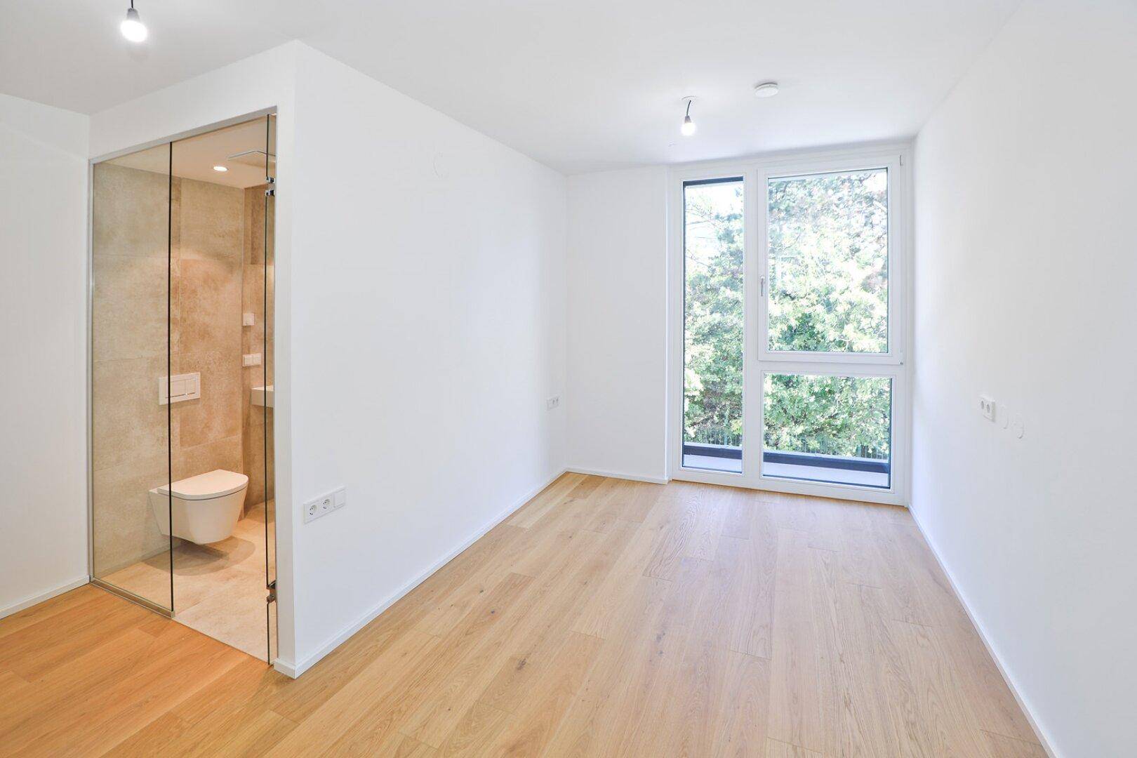 Schlafzimmer mit Holzboden und direktem Zugang zu einem modernen Badezimmer mit Glaswand.
