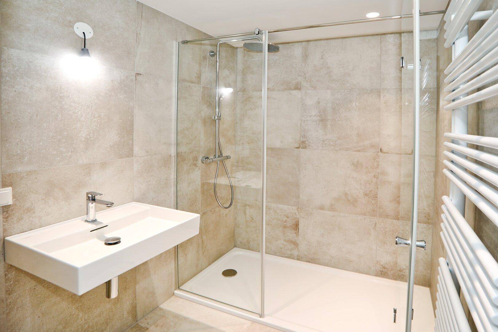 Elegantes Badezimmer mit großer Dusche, modernem Waschbecken und hellen Fliesen in Beige.