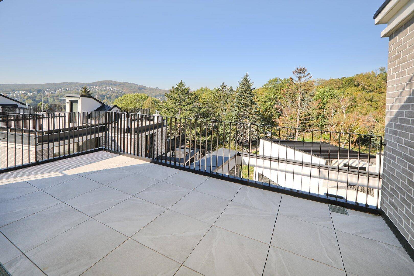Große Dachterrasse mit Fliesenboden und Panoramablick über die hügelige, grüne Landschaft.