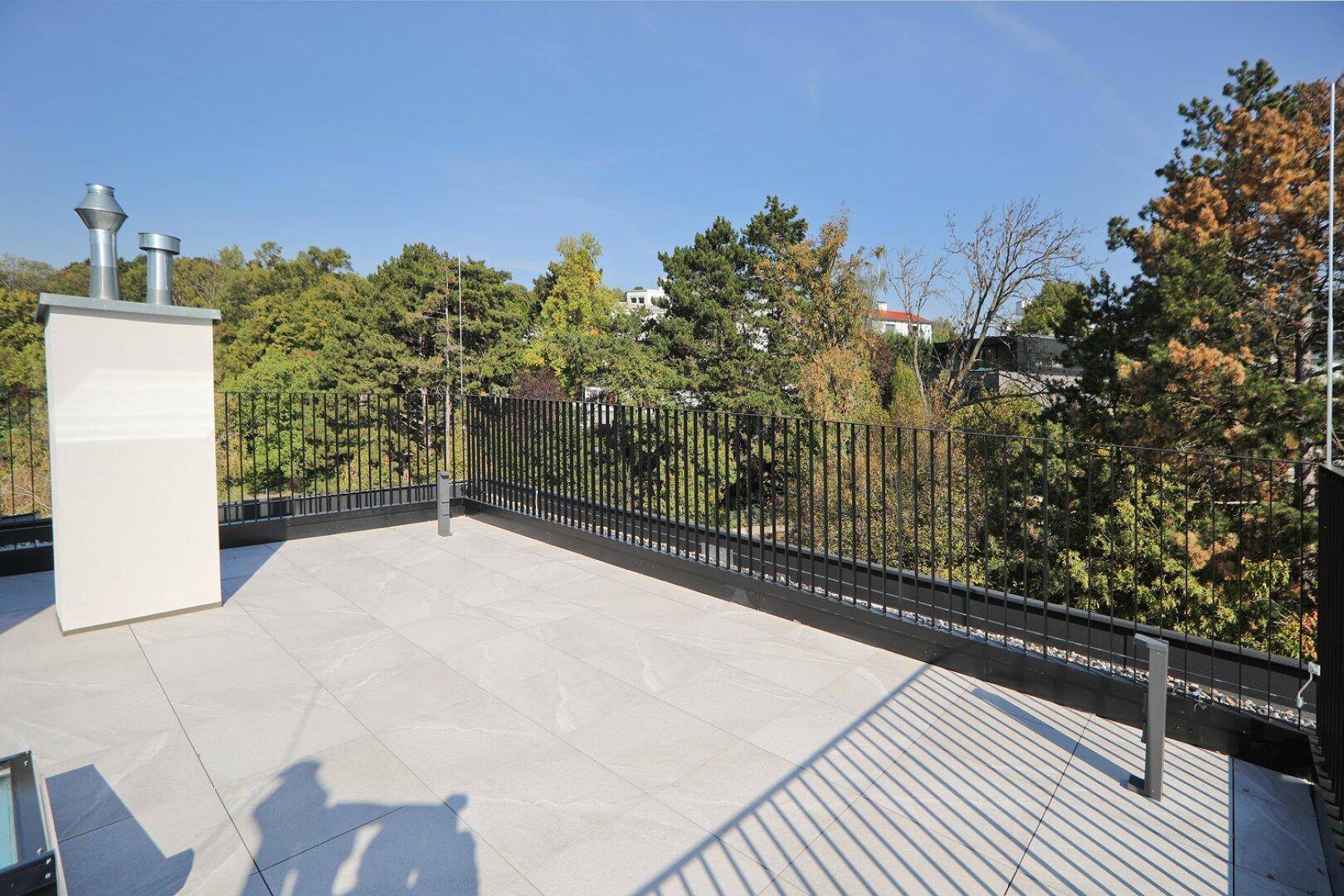 Dachterrasse mit Kamin und weitem Blick über die Baumwipfel und die umliegende Landschaft.