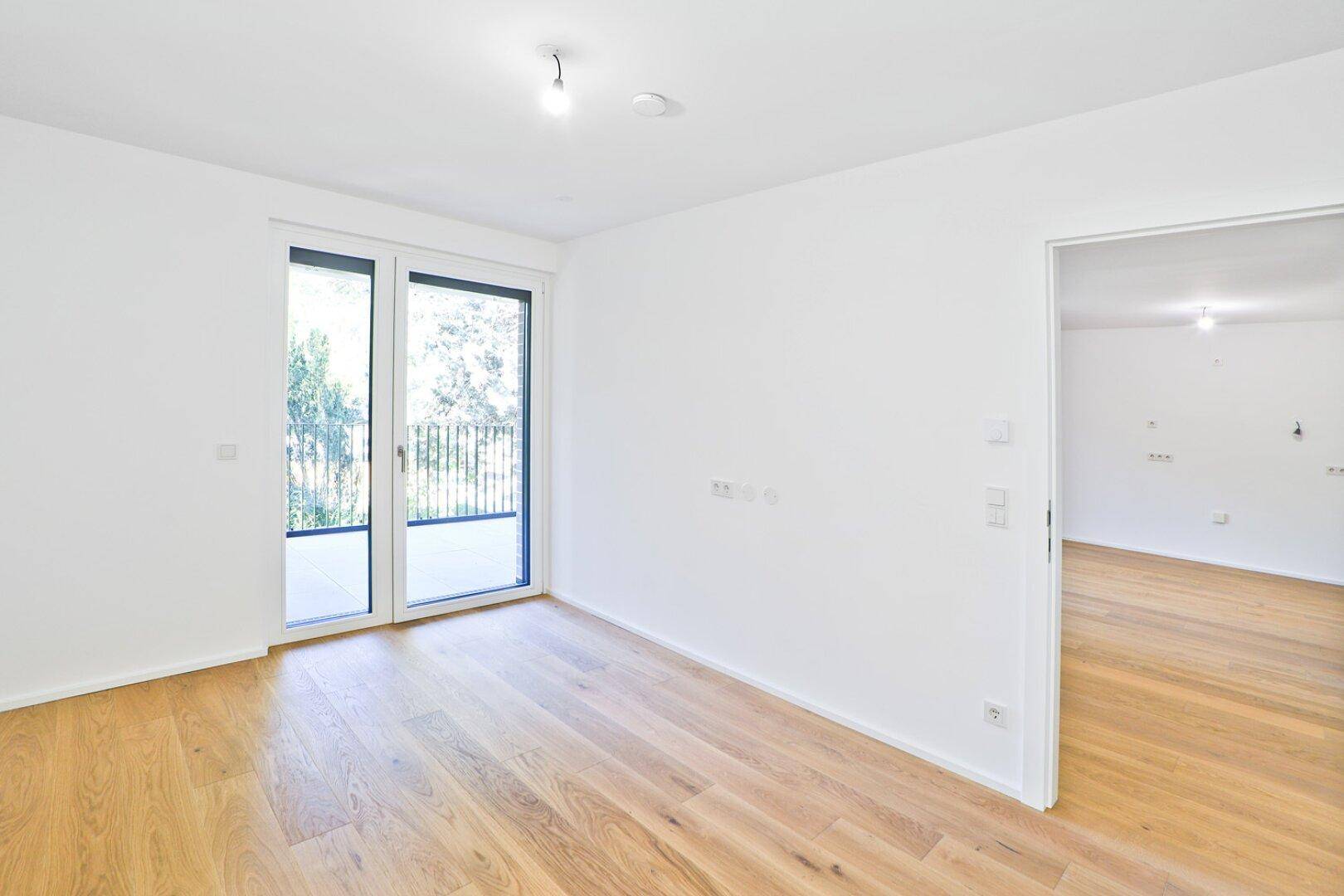 Geräumiges Zimmer mit hellem Parkettboden und Schiebetür zum Balkon, ideal für individuelle Gestaltung.