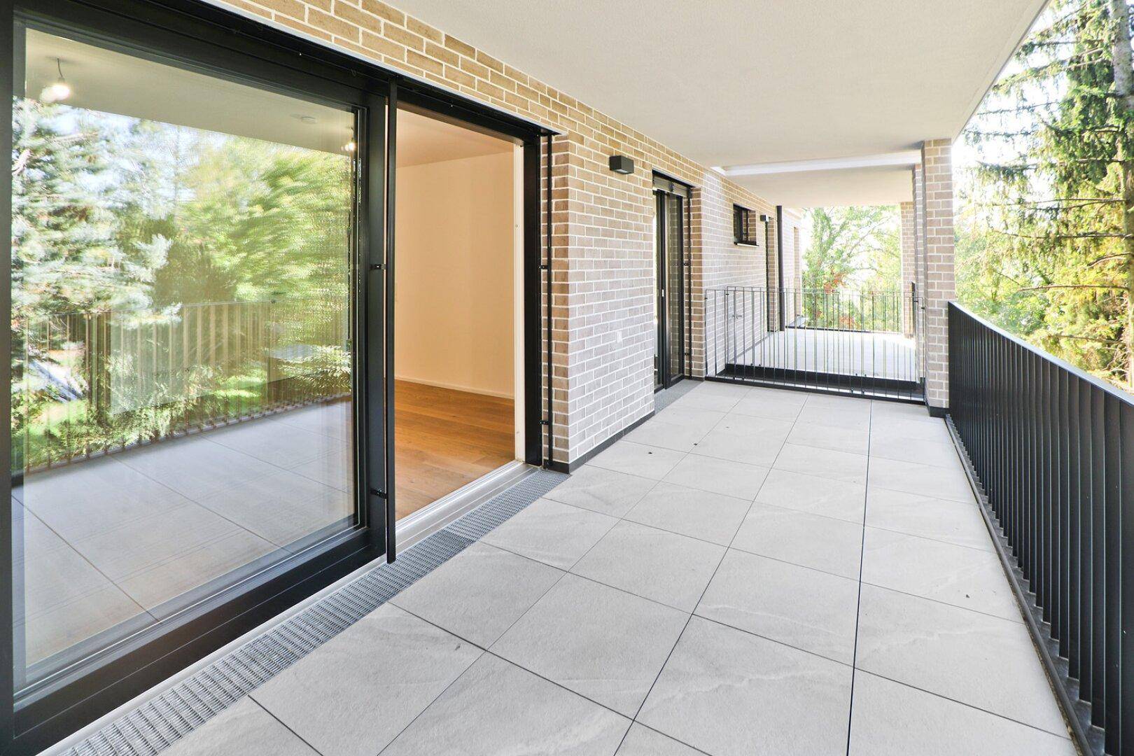 Großer, gefliester Balkon mit Blick ins Grüne und Zugang zu den Innenräumen.
