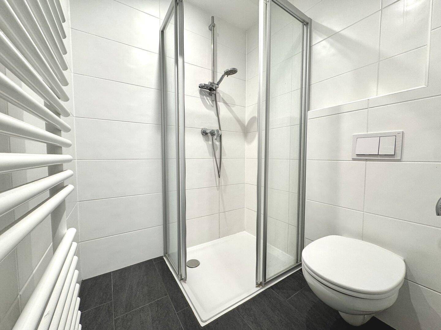 Modernes Badezimmer mit Dusche, WC und Handtuchheizkörper in weiß-grauem Design.