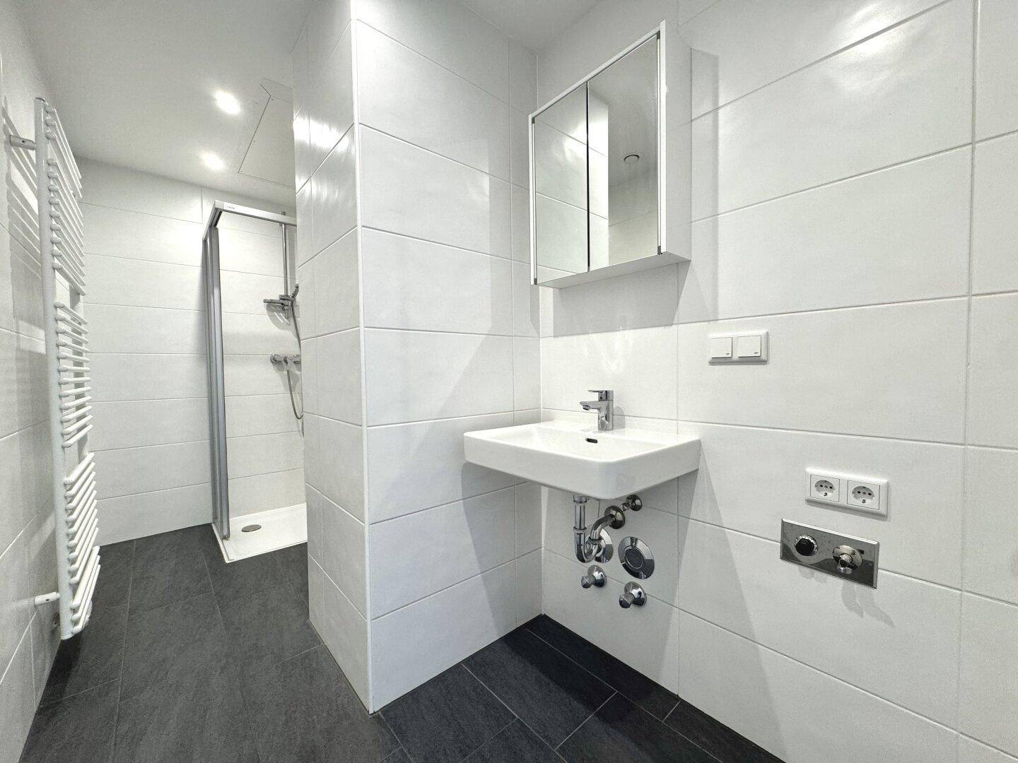 Modernes Badezimmer mit weißen Fliesen, Dusche, Waschbecken und Handtuchheizkörper.