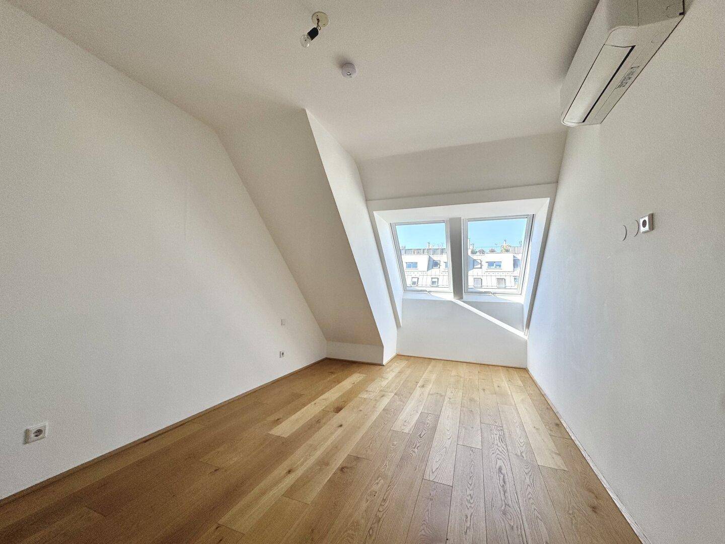 Heller Raum im Dachgeschoss mit Parkettboden, schrägen Wänden und großem Dachfenster.