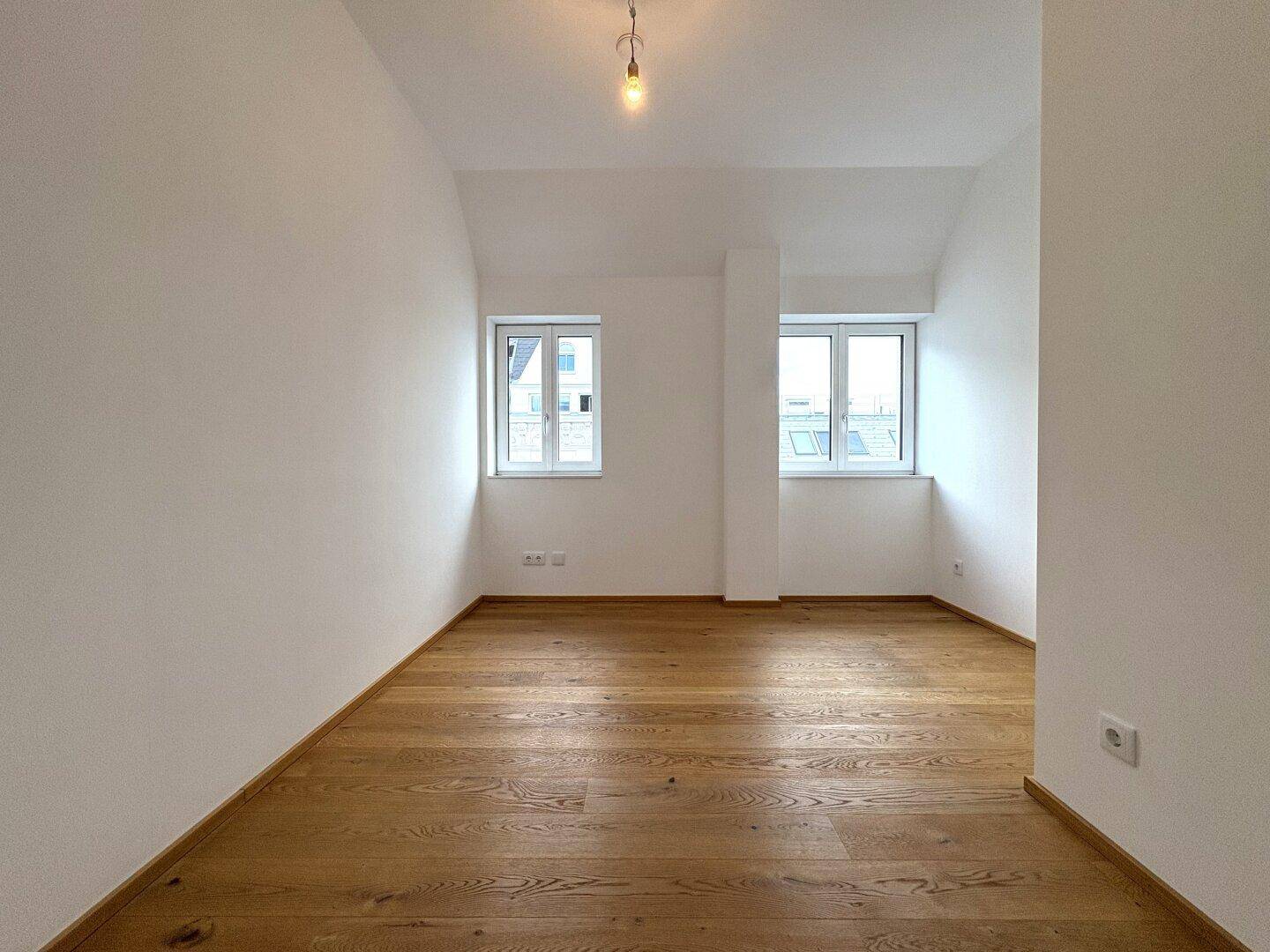 Helles Schlafzimmer mit zwei Fenstern und warmem Holzparkett, bietet eine ruhige Rückzugsmöglichkeit.