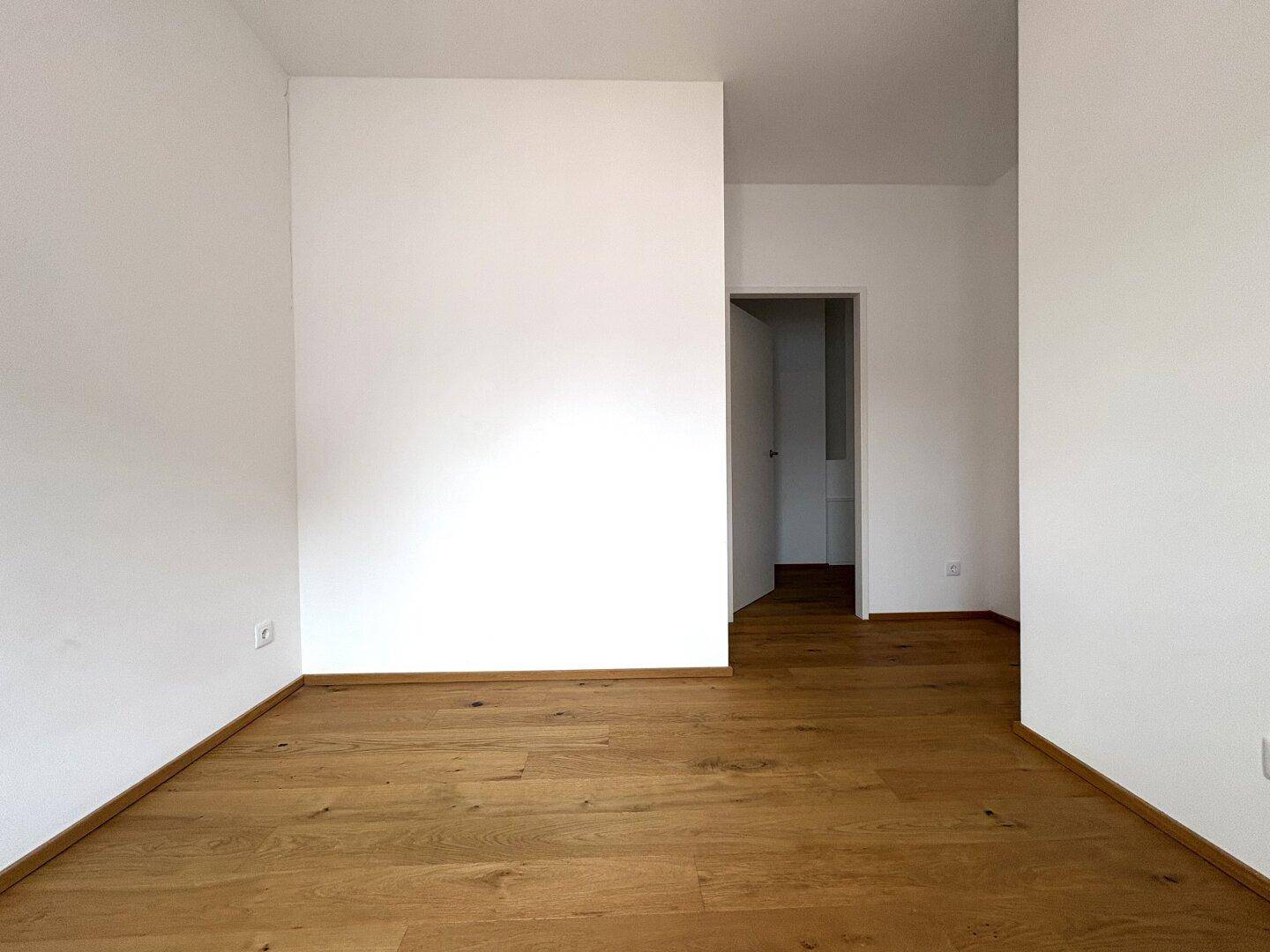 Leeres Zimmer mit Parkettboden und weiß gestrichenen Wänden, vielseitig nutzbar als Schlaf- oder Arbeitszimmer.