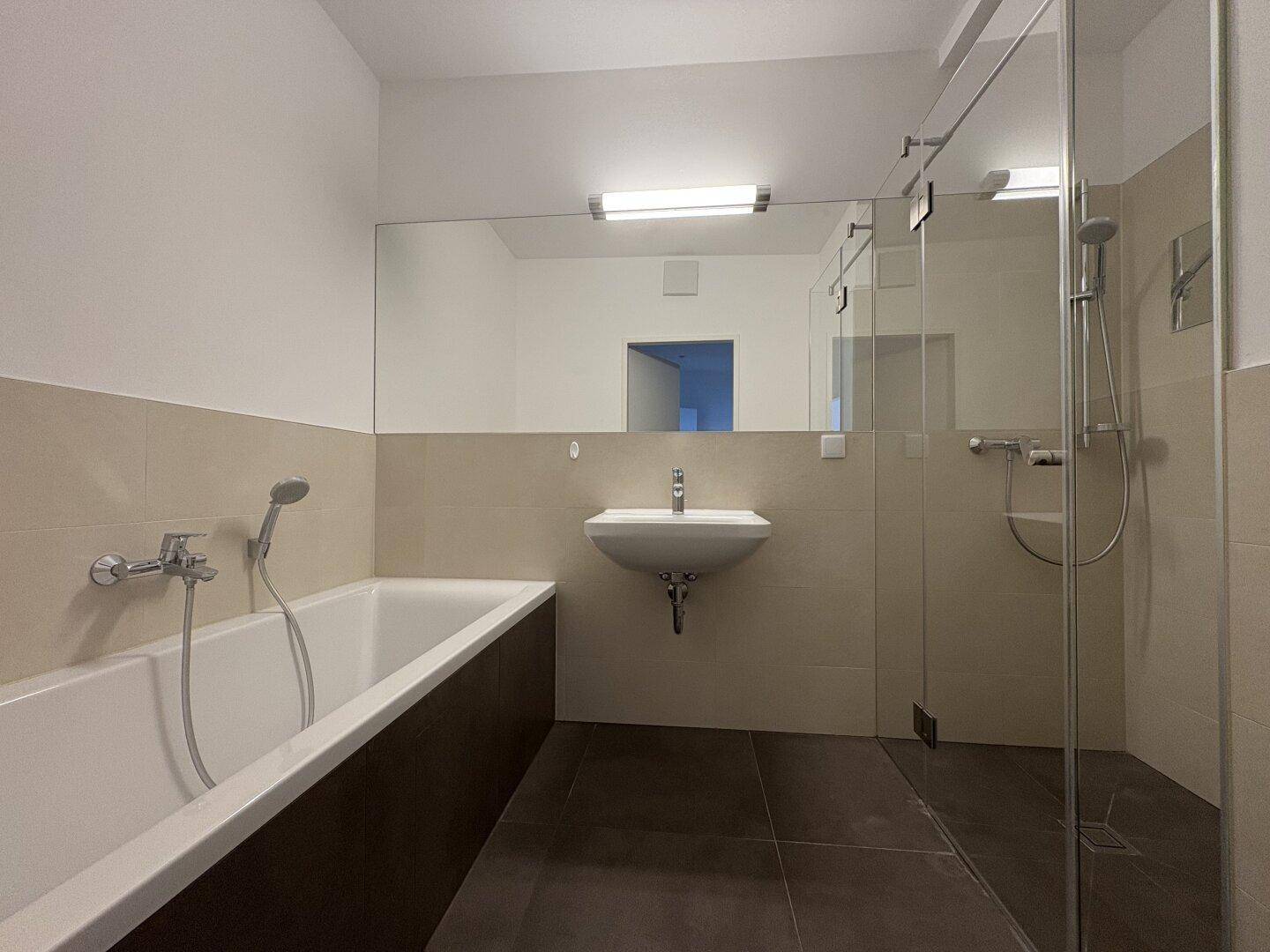 Modernes Badezimmer mit Badewanne, Duschkabine und großem Spiegel, in hellen Farbtönen gehalten.