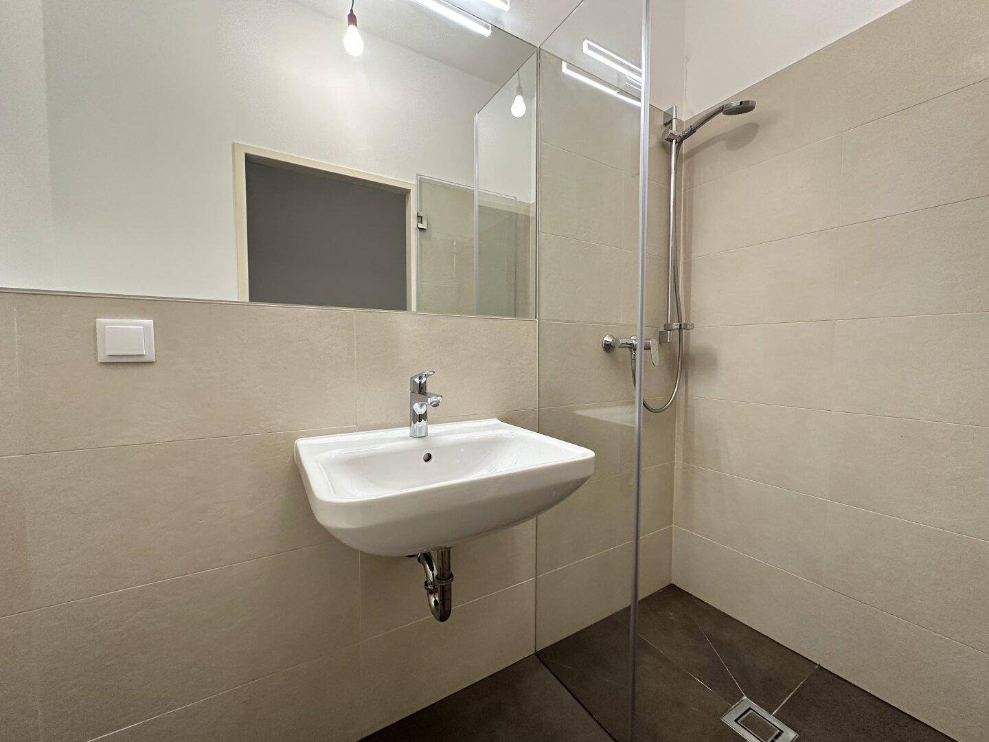 Modernes Badezimmer mit beigefarbenen Fliesen, Einzelwaschbecken und einer begehbaren Dusche.