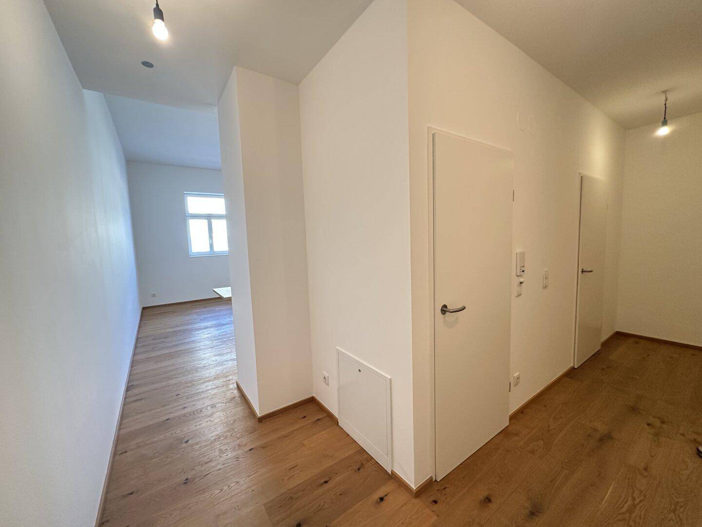 Heller Flur mit Holzfußboden und weißen Wänden, der zu weiteren Räumen führt.