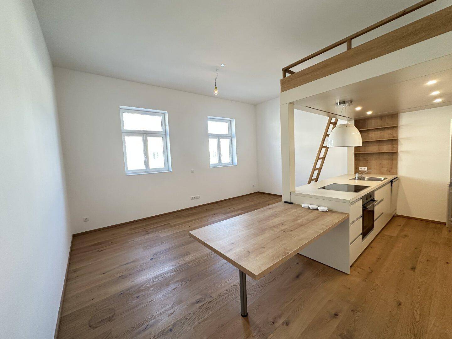 Offener Wohnbereich mit integrierter Küchenzeile, ausziehbarem Tisch und zwei Fenstern für viel Tageslicht.